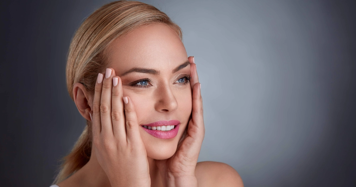 Woman with blonde hair smiles and frames her face with her hands, highlighting skin tightening in Middletown, NY.